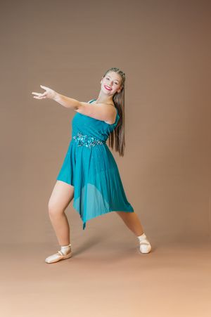 Performer in turquoise dress strikes dynamic dance pose with outstretched arms.