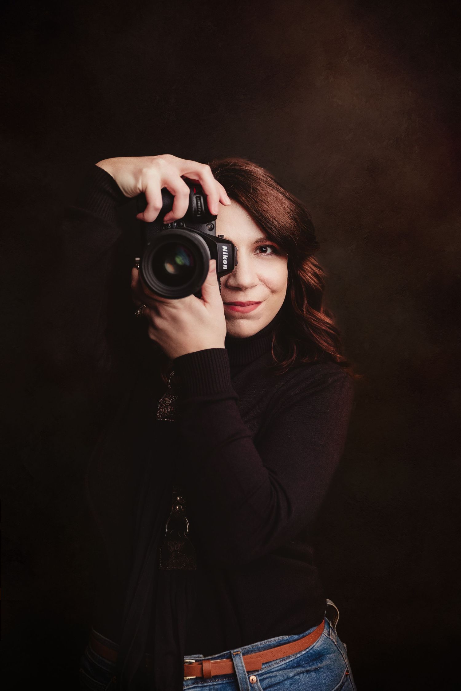 Studio portrait of a person in a black turtleneck and jeans against a dark background.