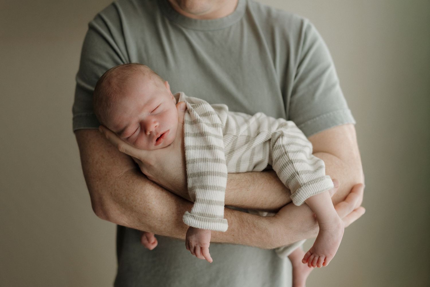 A sleeping infant wearing light colored clothing lies peacefully on a white bed with black metal headboard.
