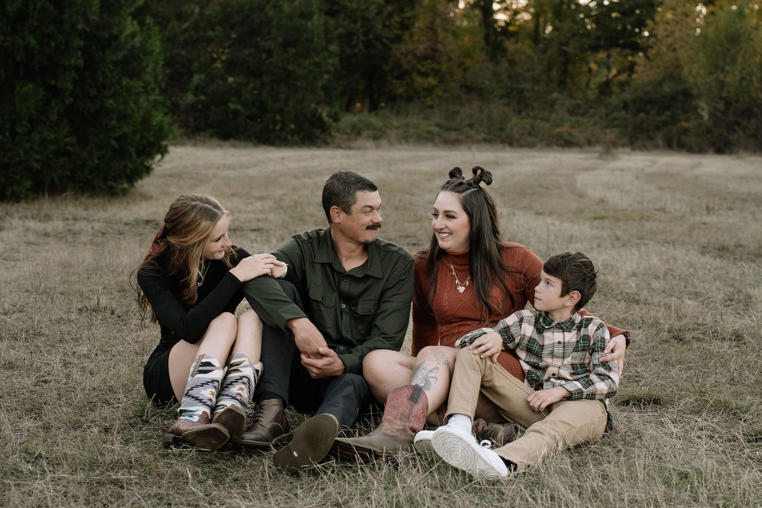Family relaxes together on grassy hillside during golden hour sunset photo session.