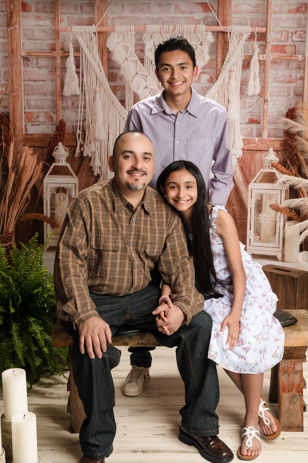 A portrait of a family posing together in a rustic setting with white macrame hangings and lantern decorations.
