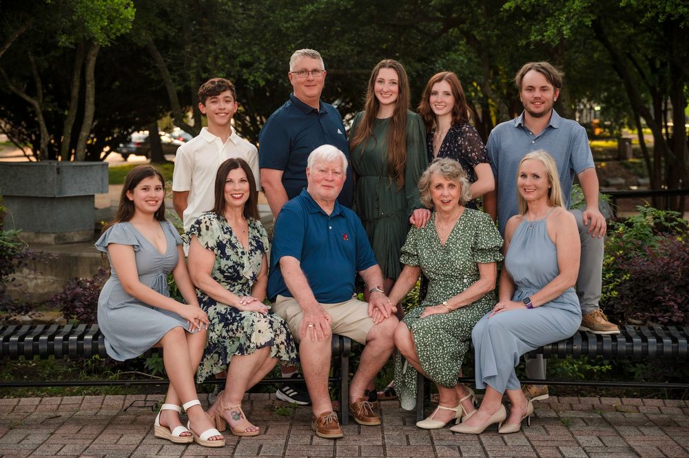 Multi-generational family portrait taken outdoors on a brick patio with lush greenery in the background.