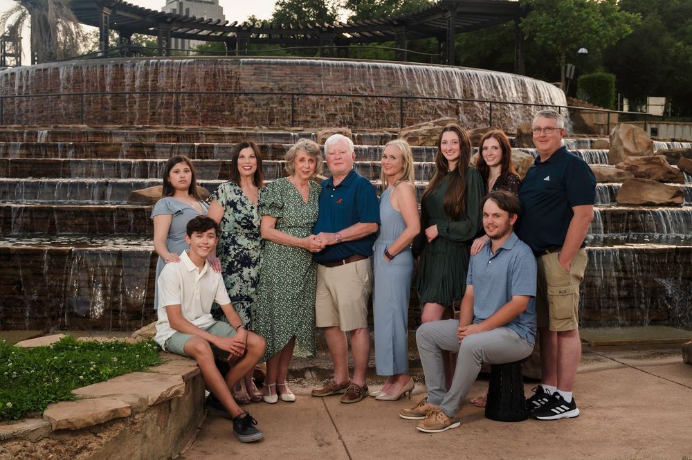 A group of people gather together for a family portrait in front of a cascading stone water fountain at sunset.