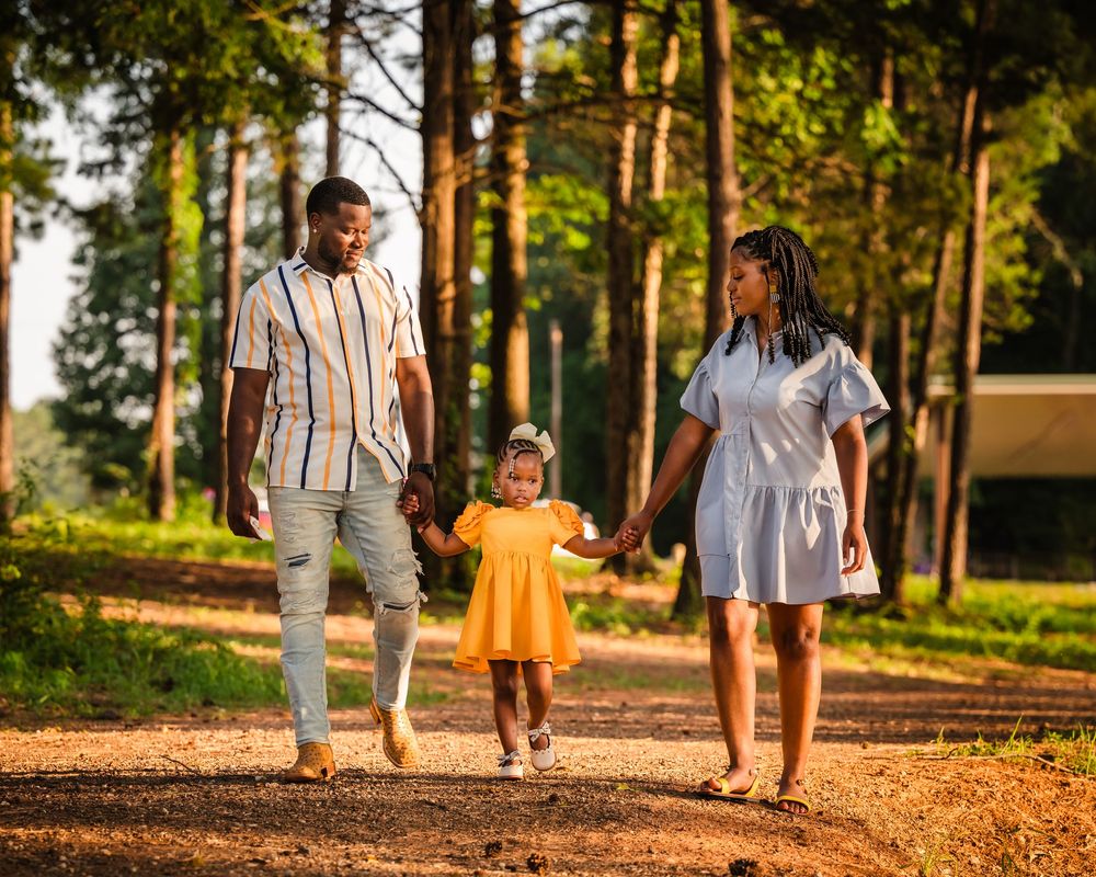 A family walks together on a sunlit forest path during golden hour.