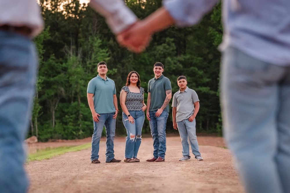 A casual group photo on a dirt road at sunset with trees in the background.