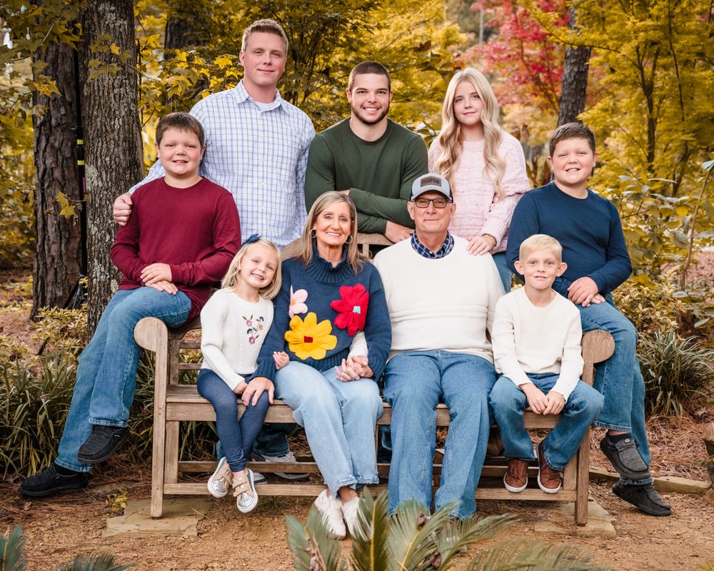A group sits together on wooden benches surrounded by vibrant fall foliage in a forest setting.