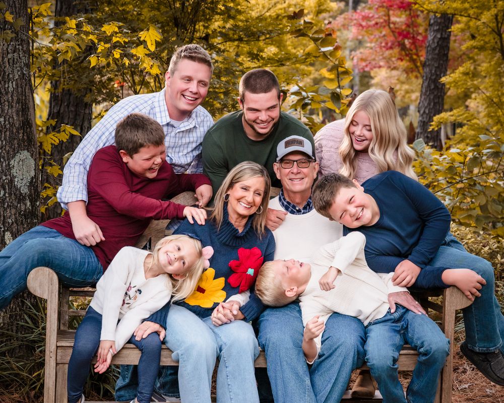 A group sits together on wooden steps surrounded by golden autumn foliage during an outdoor photo session.