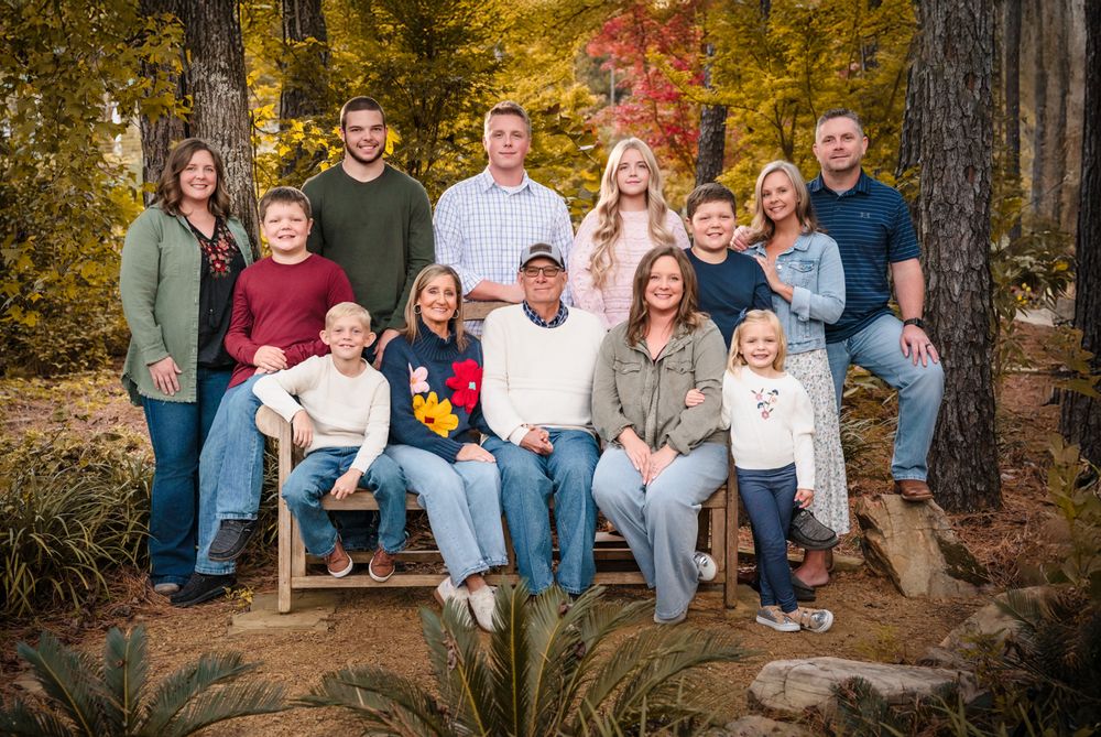 A group of people wearing casual clothing sits together outdoors on a large fallen tree trunk during autumn.