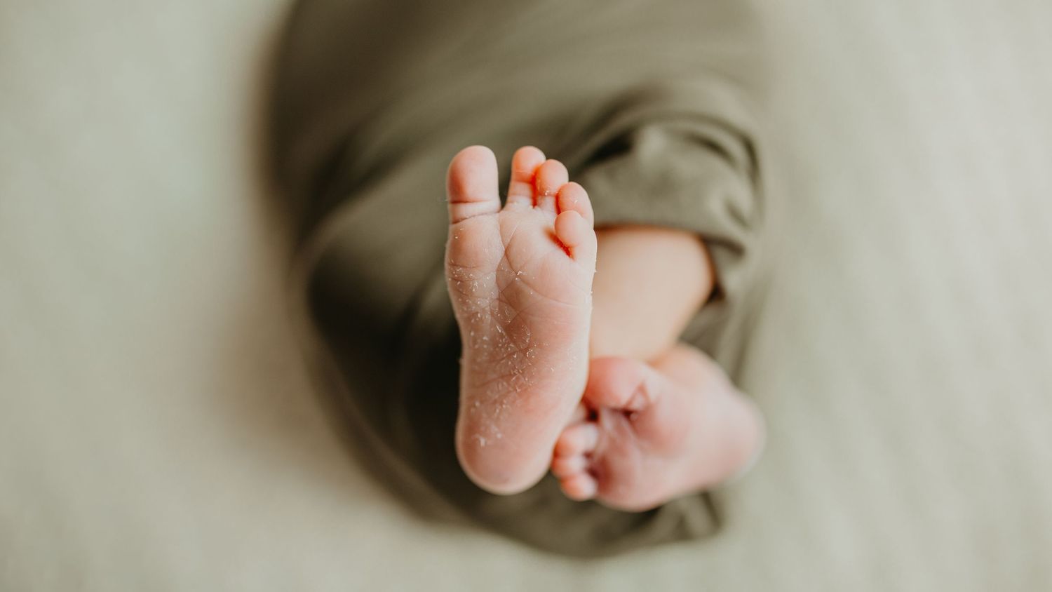 Small baby's foot wrapped in soft rust-orange fabric in a dreamy, intimate close-up portrait.