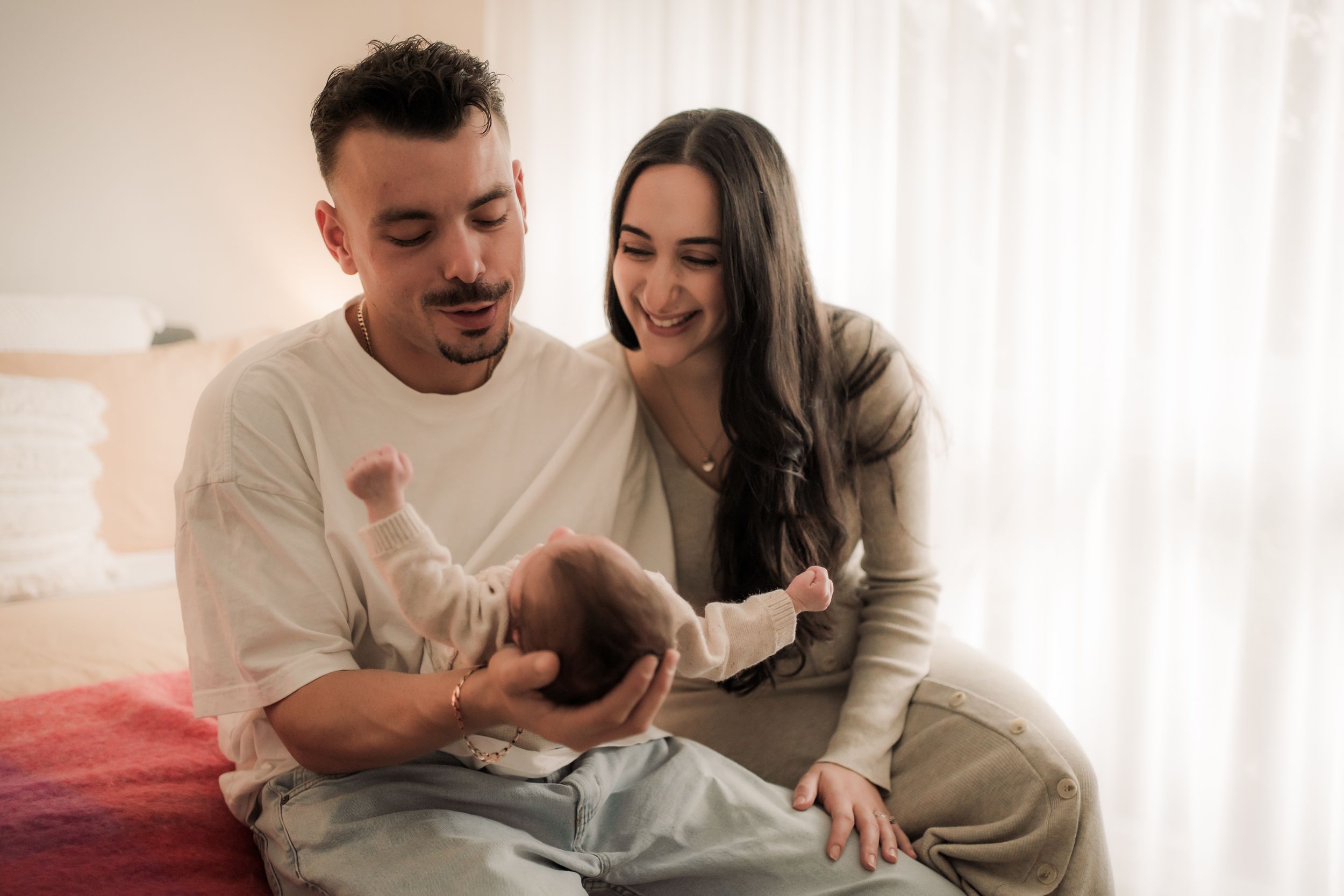 A couple wearing comfortable loungewear sits on a couch together sharing a playful moment in their bright living room.