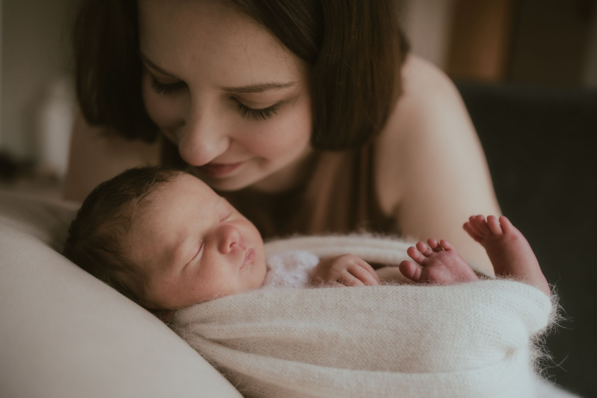 A tender moment shows a sleeping newborn baby snuggled in soft white blankets on a bed.
