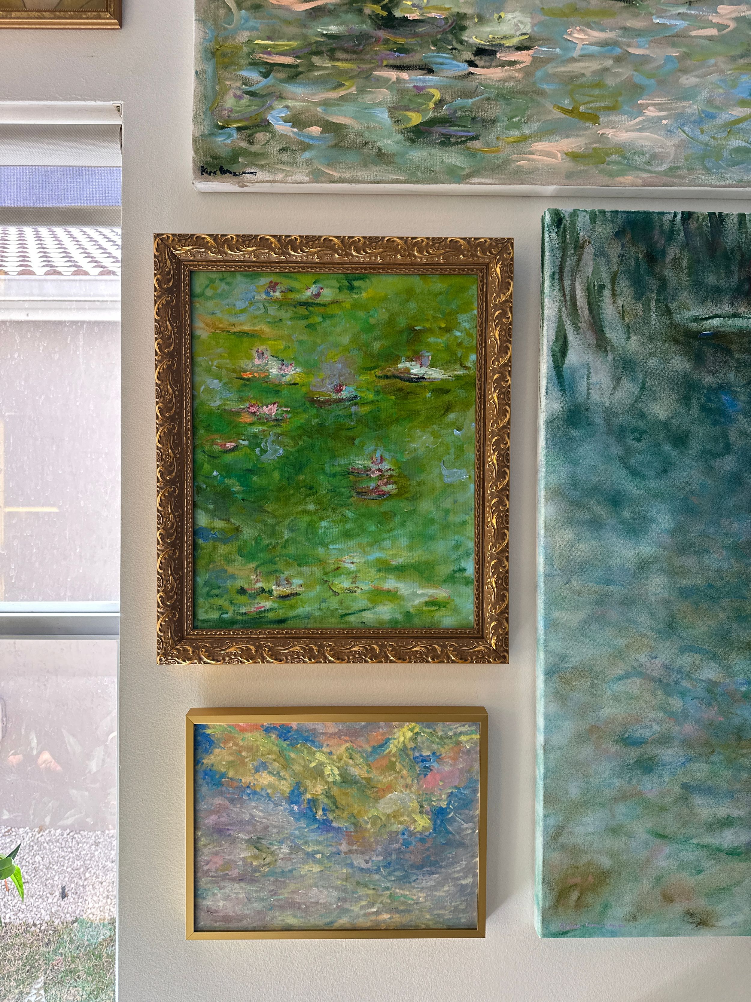 Elegant gallery wall features three Monet-style water lily paintings in ornate gold frames against a white wall.