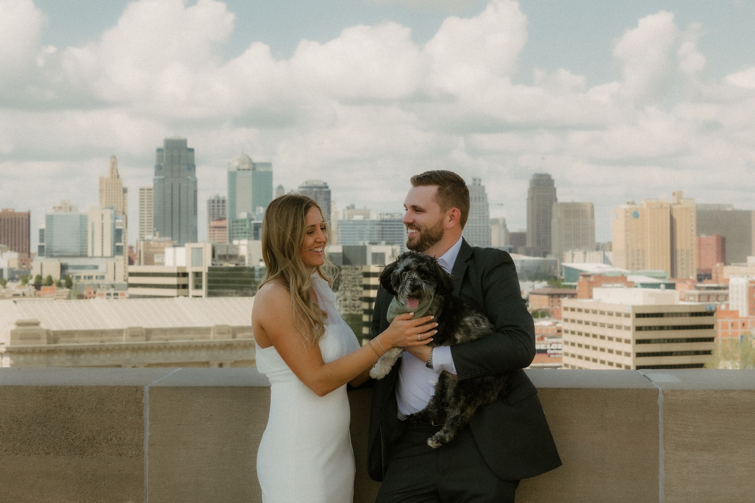 A couple shares a romantic moment on a rooftop with the Kansas City skyline in the background.