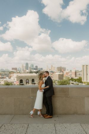 A romantic couple embraces on a rooftop overlooking the Kansas City skyline on a cloudy day.