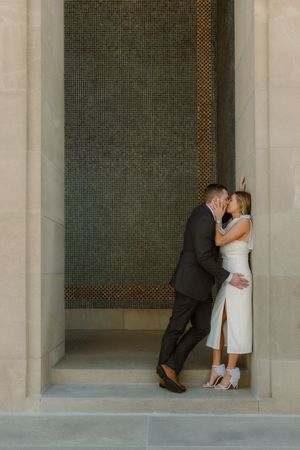 Elegant couple shares an intimate moment against a textured wall in formal attire.