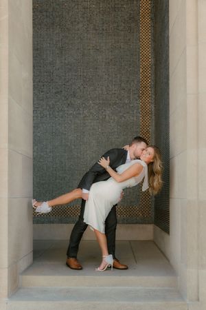 A romantic dip pose between a couple in formal attire against a modern architectural backdrop.