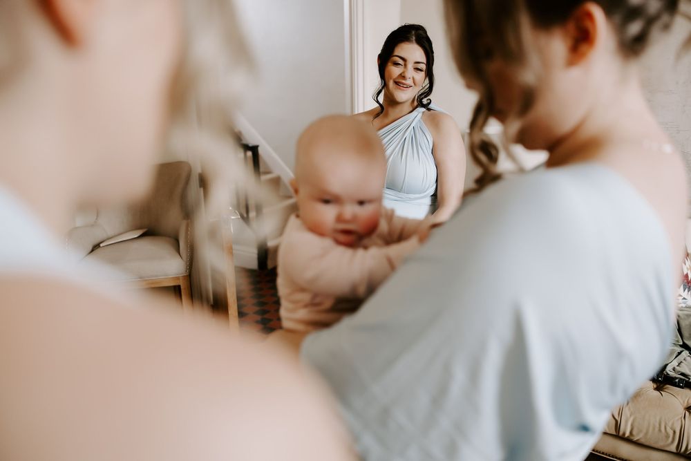 A baby is being held during a small gathering in a sunlit room.
