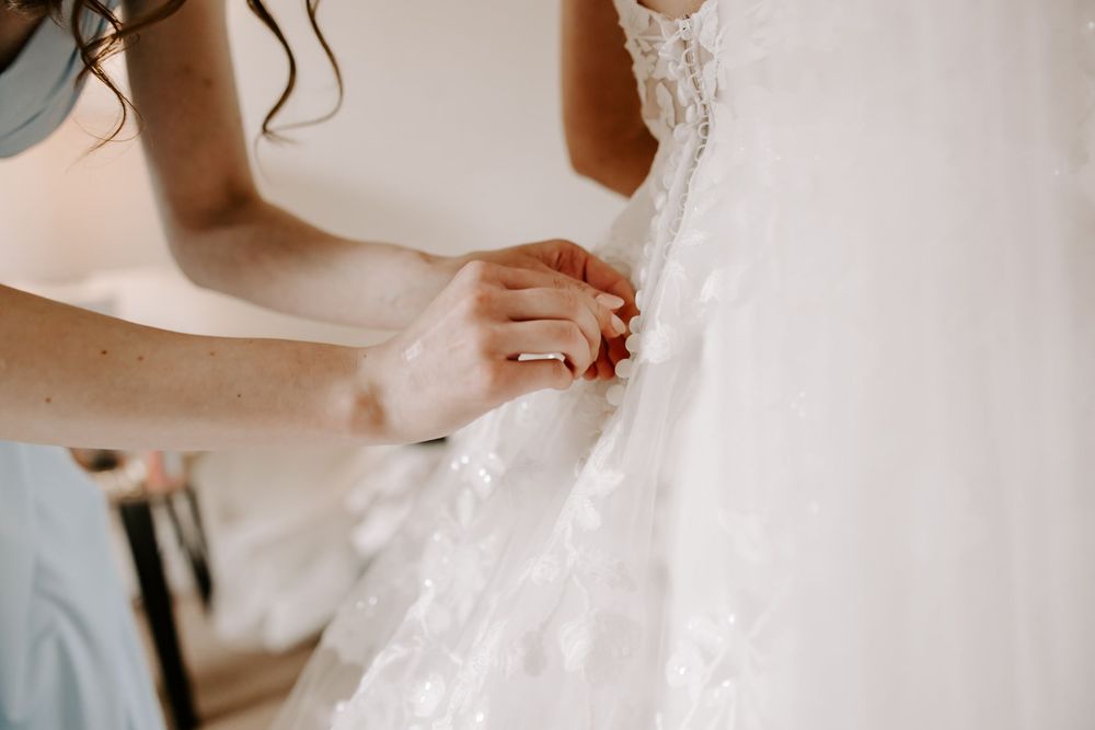 A person adjusts delicate lace details on an elegant white wedding dress sleeve.