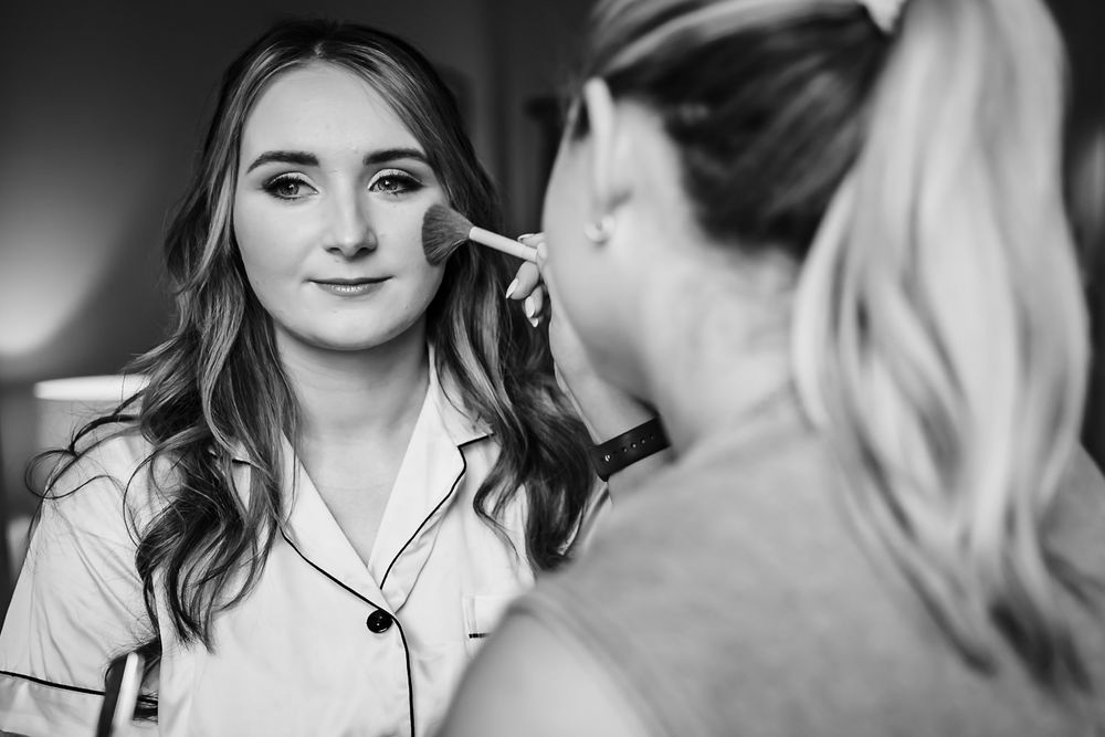 A makeup artist applies cosmetics to a client's face during a professional beauty session in black and white.
