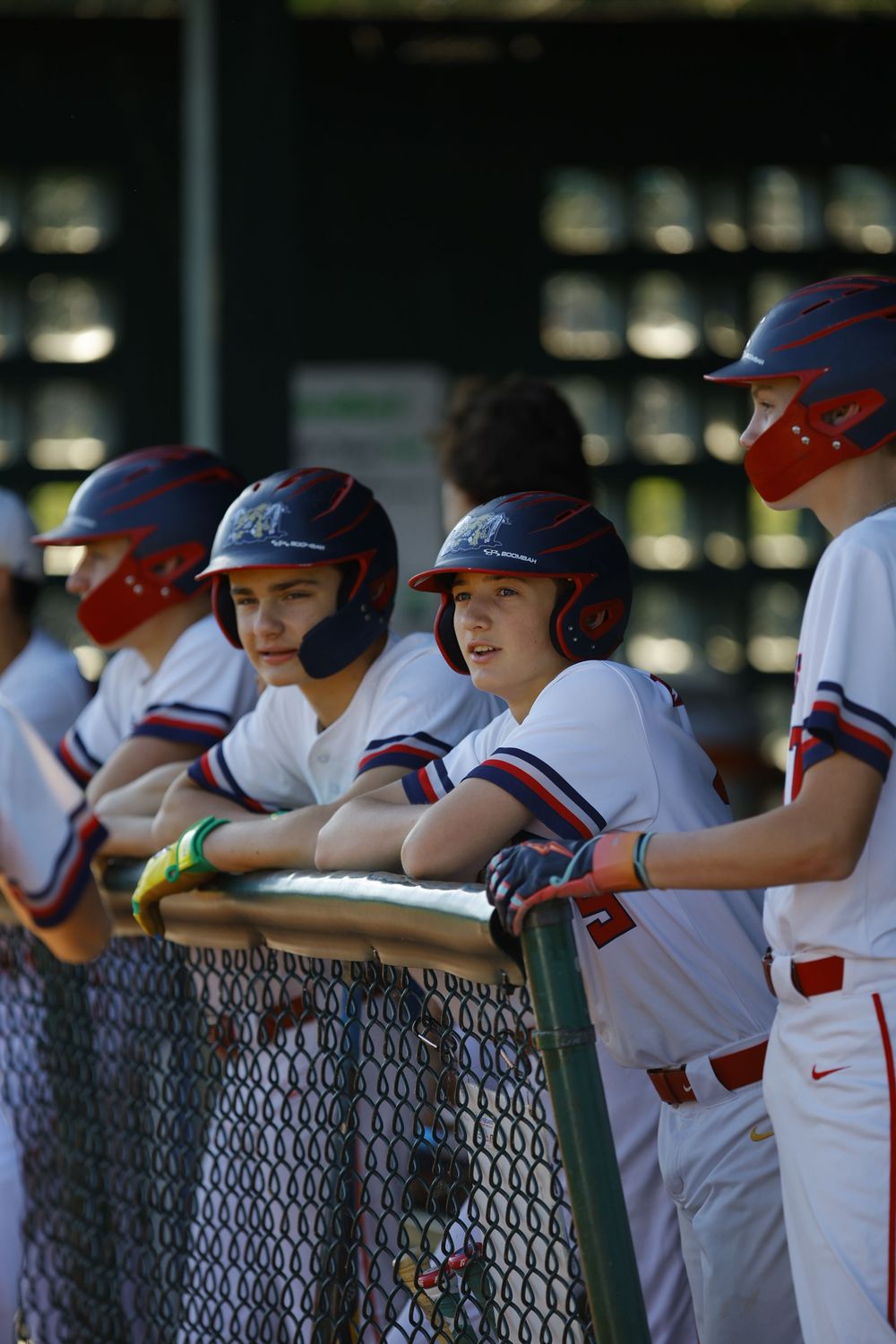 Baseball team members in white uniforms line up along dugout fence during game.