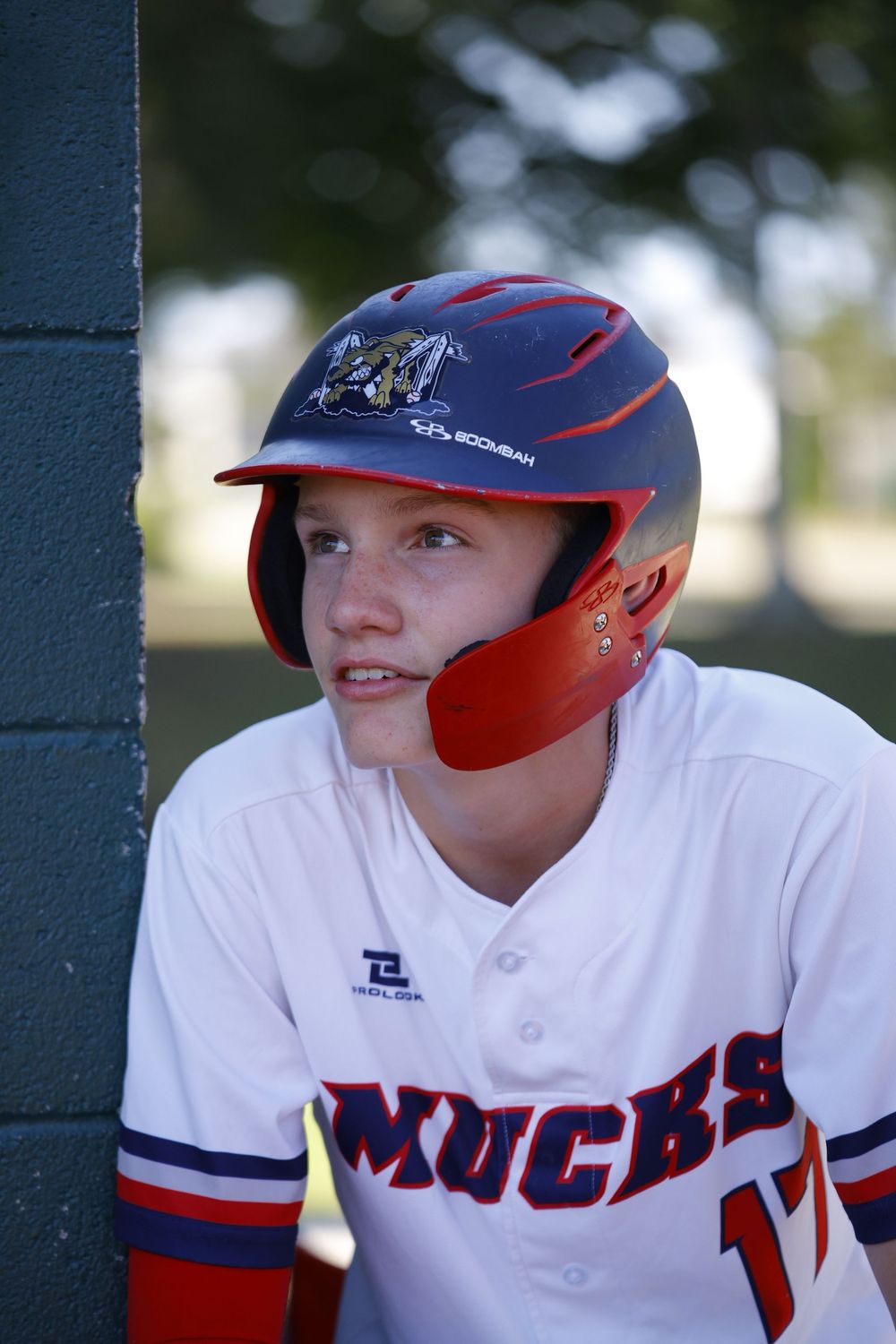 Baseball player wearing a navy and red batting helmet sits in the dugout wearing Knights team uniform.