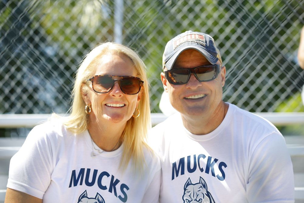 Couple wearing matching Mucks team t-shirts smile at baseball field.