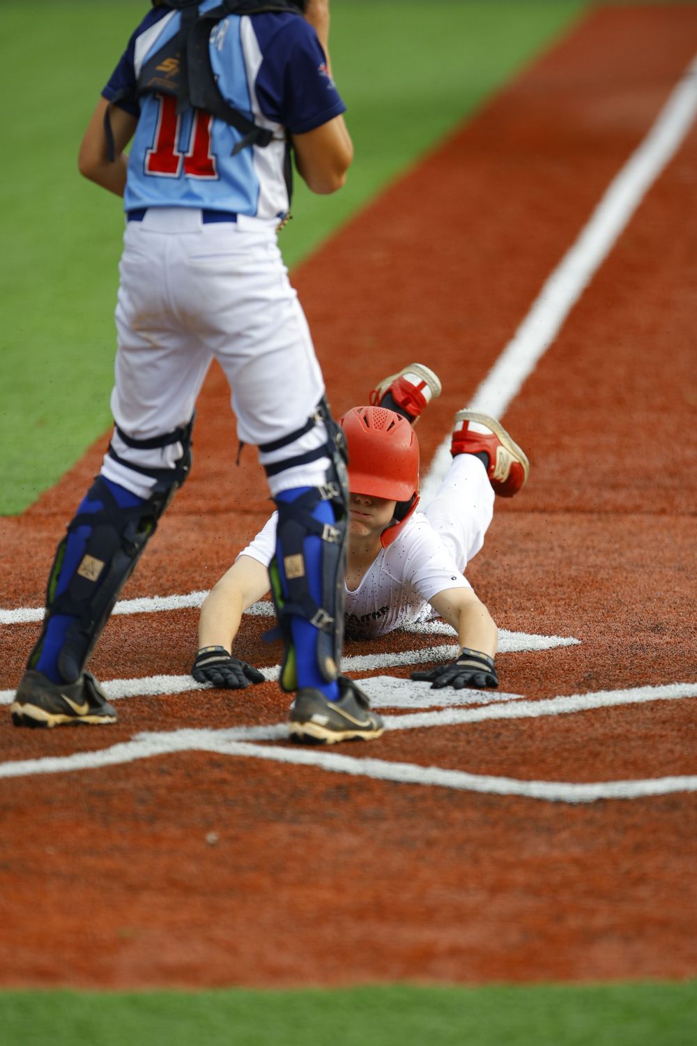 Baseball runner slides into home plate while catcher stands ready for the play.