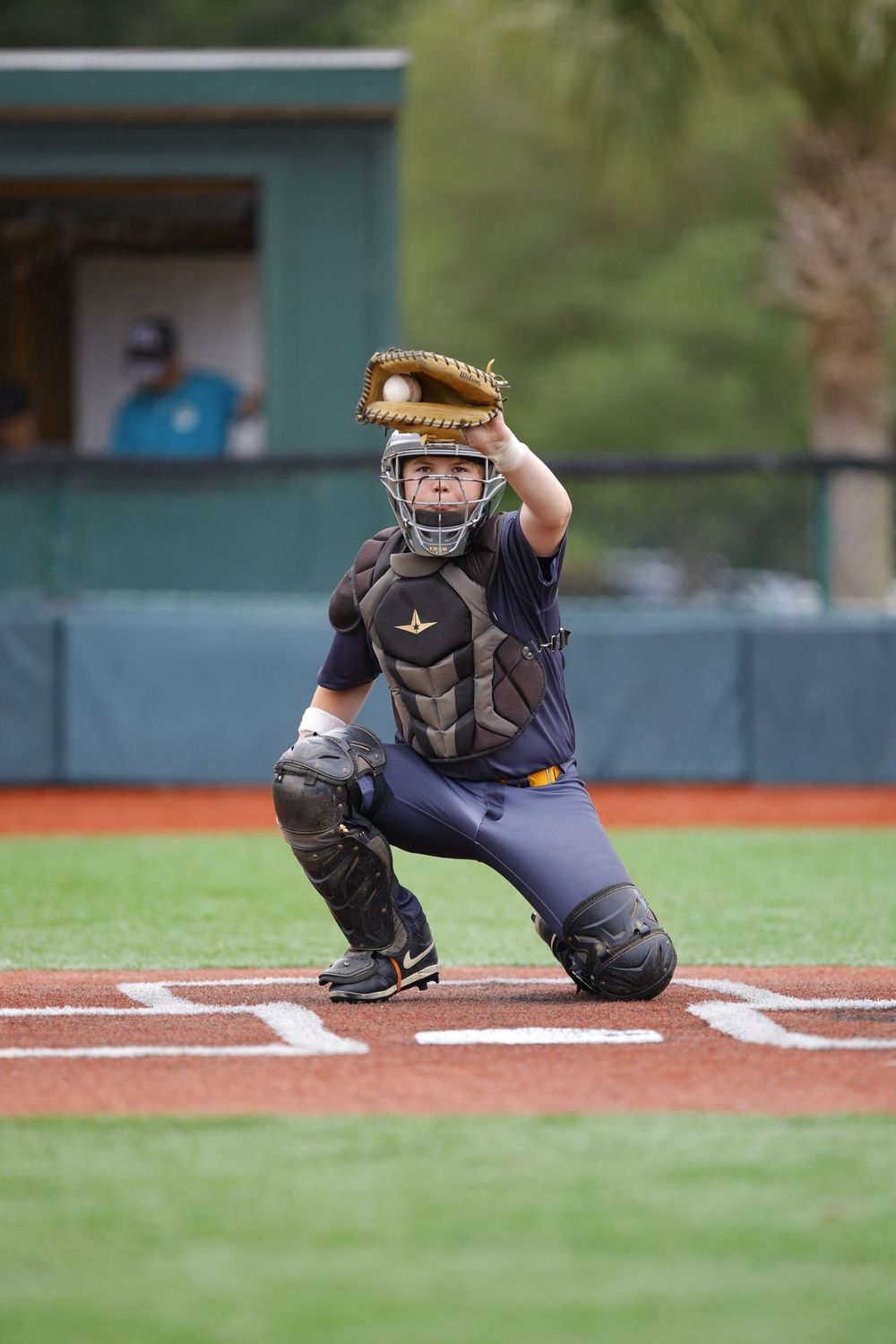Youth catcher in protective gear crouches behind home plate ready for the pitch.