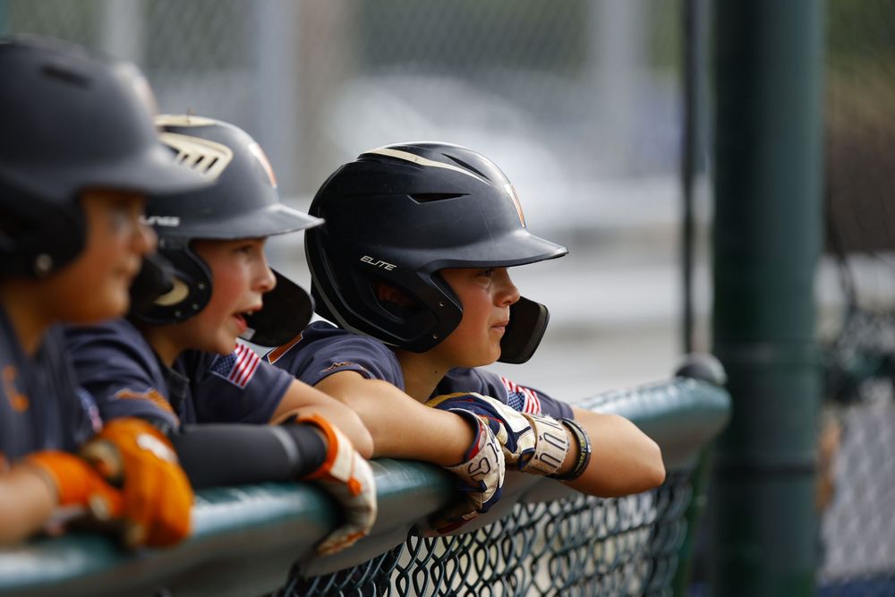 Baseball players in navy helmets lean on dugout fence watching the game.