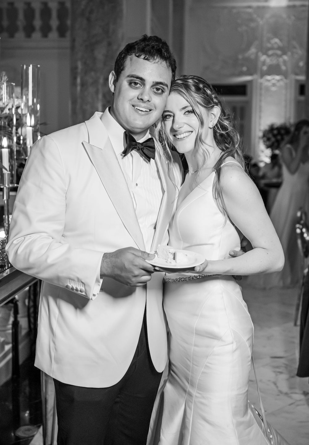 Black and white wedding photo of newlyweds in elegant attire smiling together at formal reception venue.