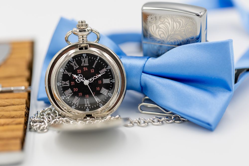 Vintage pocket watch and blue bow tie arranged as wedding accessories.