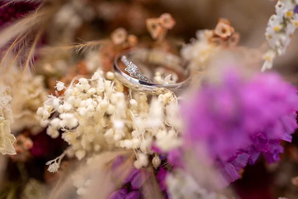 Wedding ring macro shot surrounded by dried flowers in soft focus.