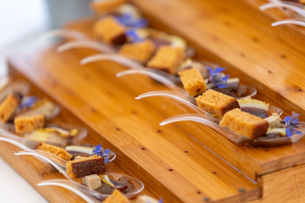 Elegantly plated appetizers on wooden serving boards with small purple flowers and white garnishes.