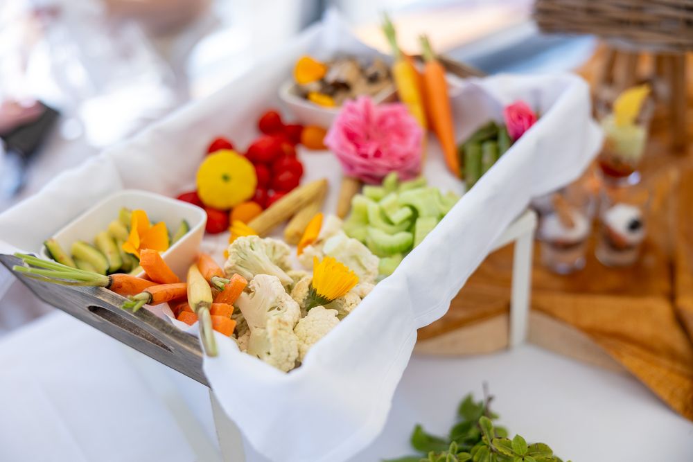 Fresh vegetable and appetizer platter with colorful carrots, flowers and greens arranged on white serving trays.