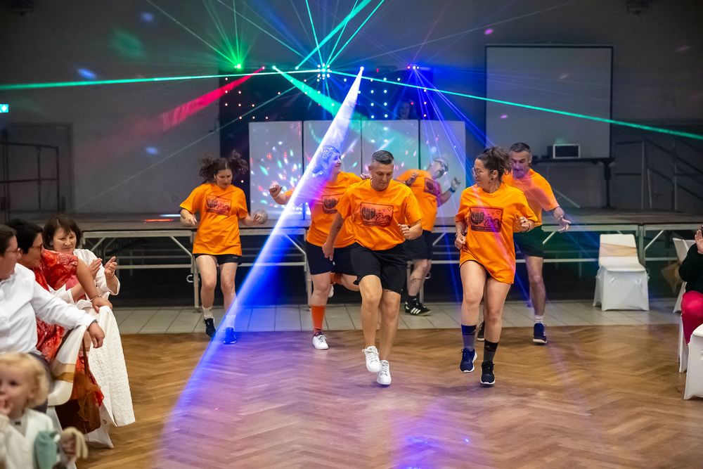 Dancers in bright orange shirts perform under blue and green laser lights.