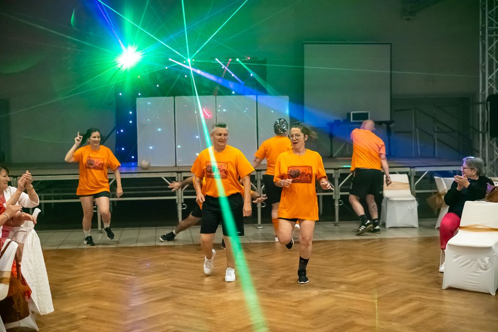 People in orange shirts dancing under colorful laser lights at an event.