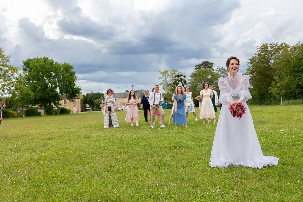 A wedding party stands on a grassy hill under dramatic cloudy skies during an outdoor celebration.