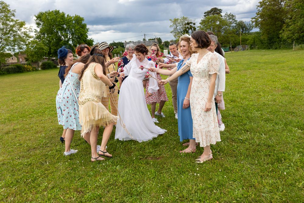 A festive group dances in a circle on green grass during an outdoor celebration.