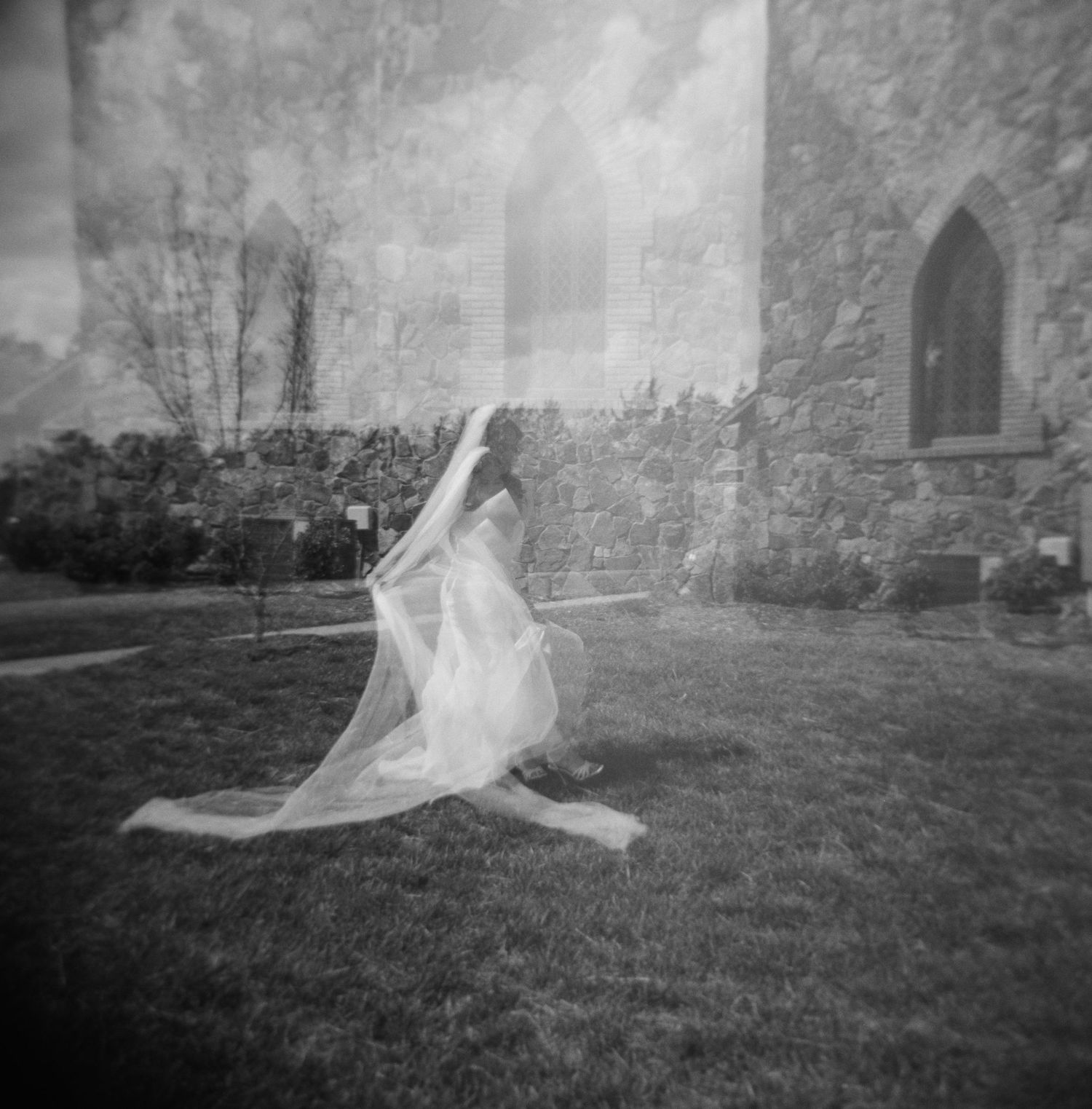 An ethereal black and white photo of a flowing veil dancing in the wind outside a stone church.