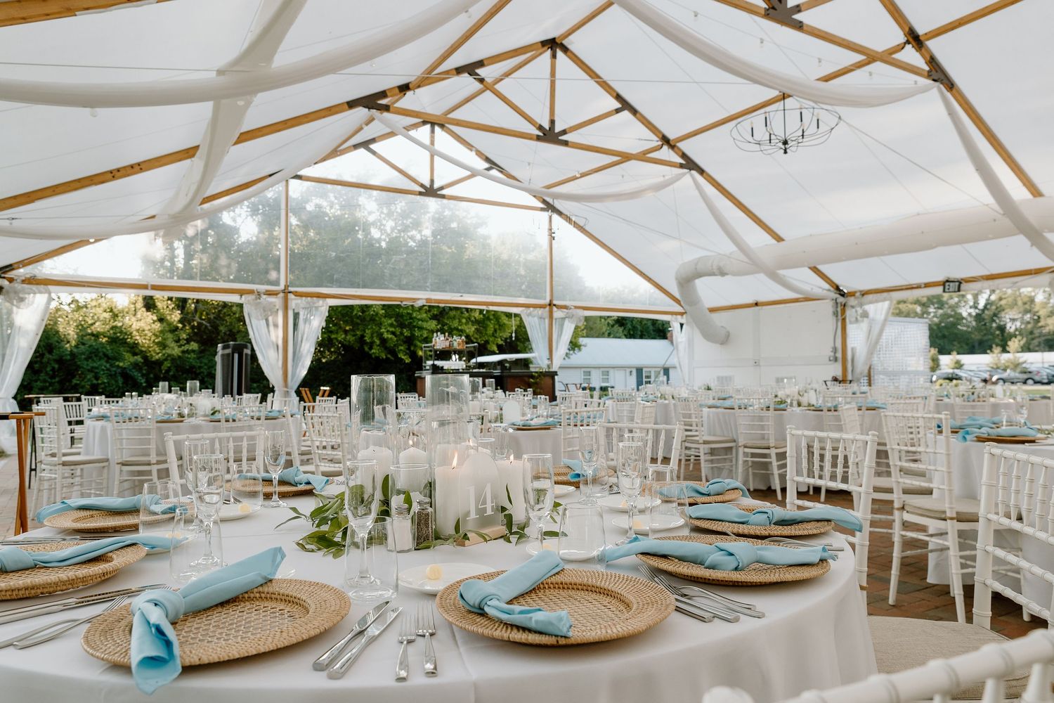 Elegant white tent reception setup with chiavari chairs and blue accented place settings for a wedding celebration.