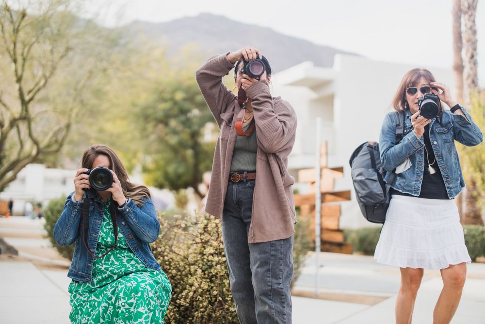 Three photographers taking pictures outdoors with cameras in an urban setting.