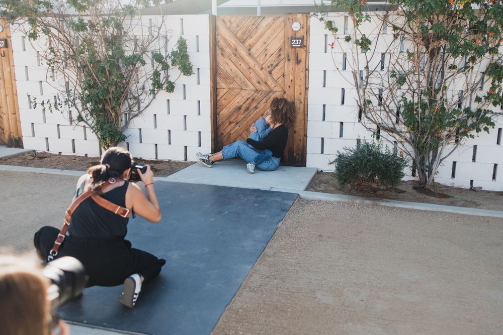 A photographer crouching to take photos near a decorative white fence and plants.