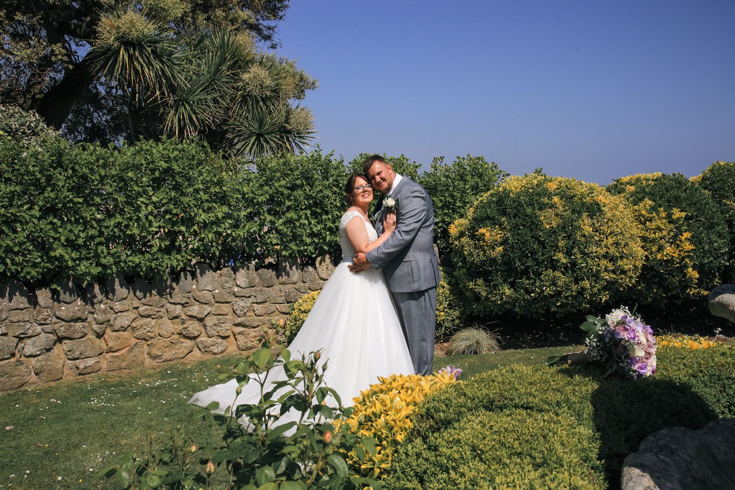 Couple seated at decorated wedding table with greenery and red floral centerpiece.
