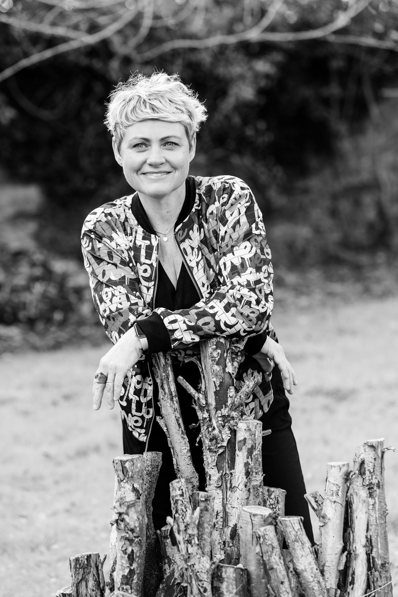 Black and white portrait of someone in patterned jacket leaning on rustic wood logs.