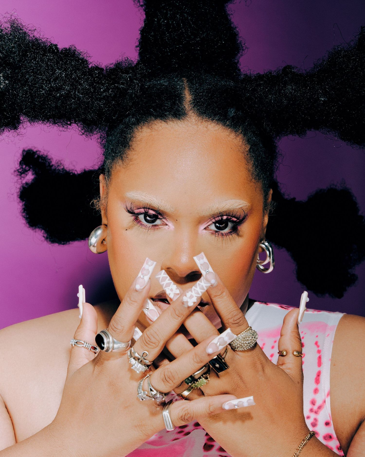 Artistic portrait with vibrant purple background featuring unique hairstyle and multiple rings on hands.