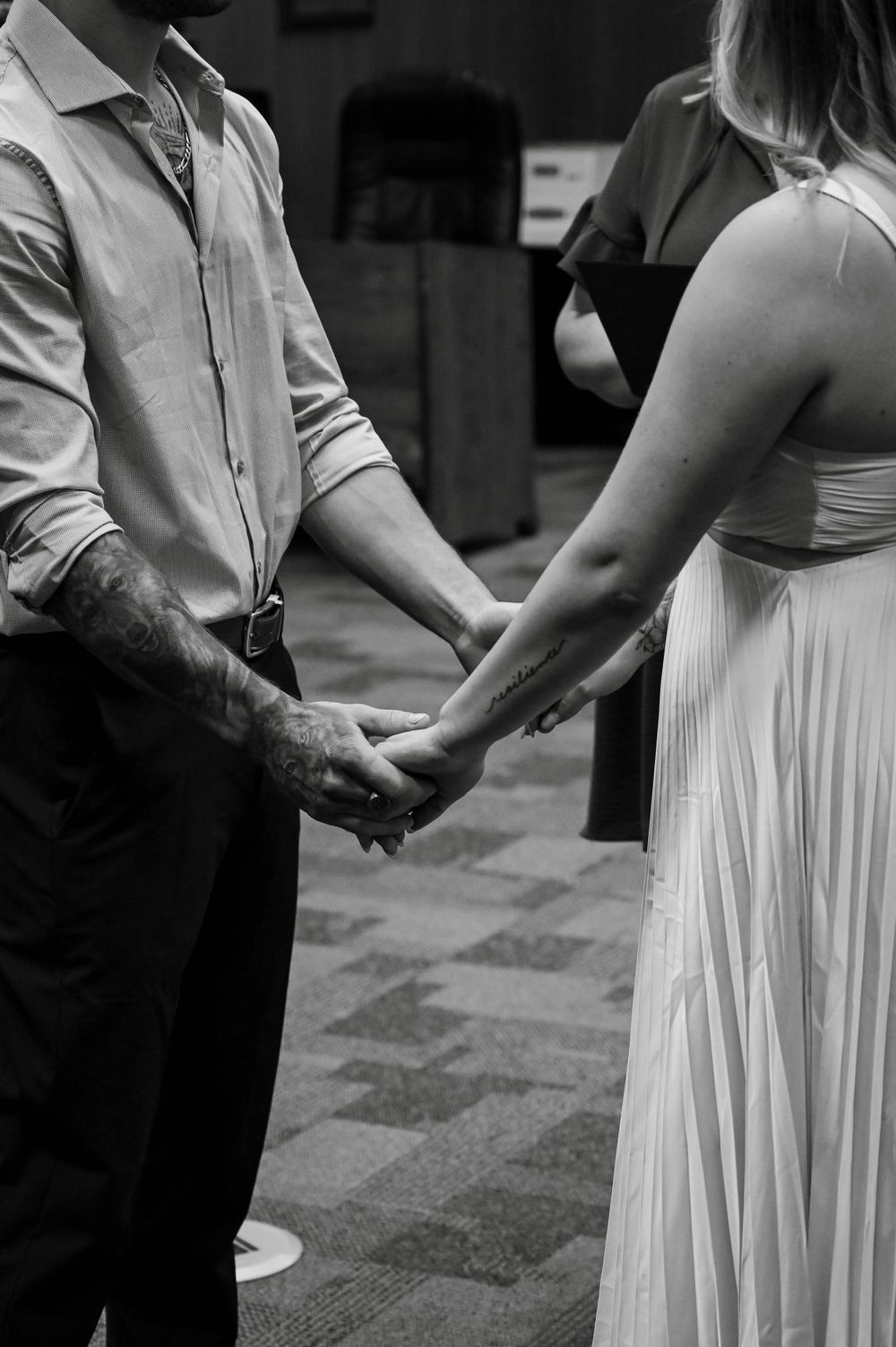 A black and white photo of a couple holding hands during what appears to be a wedding ceremony.