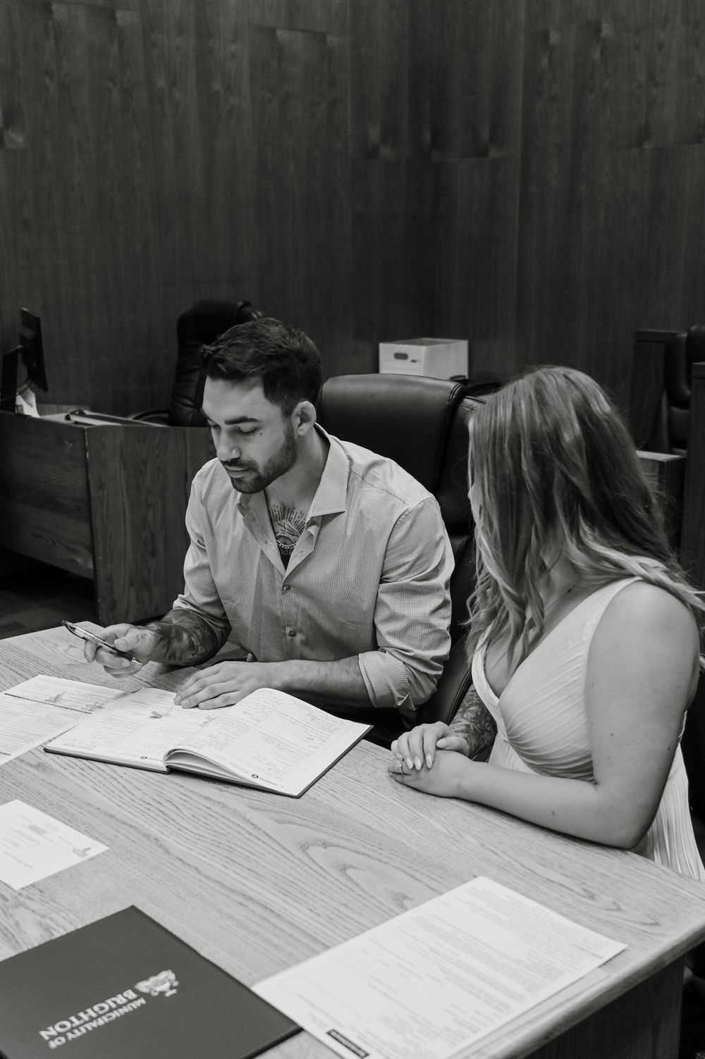 A black and white photo shows two people studying together at a wooden table with documents and folders spread out.