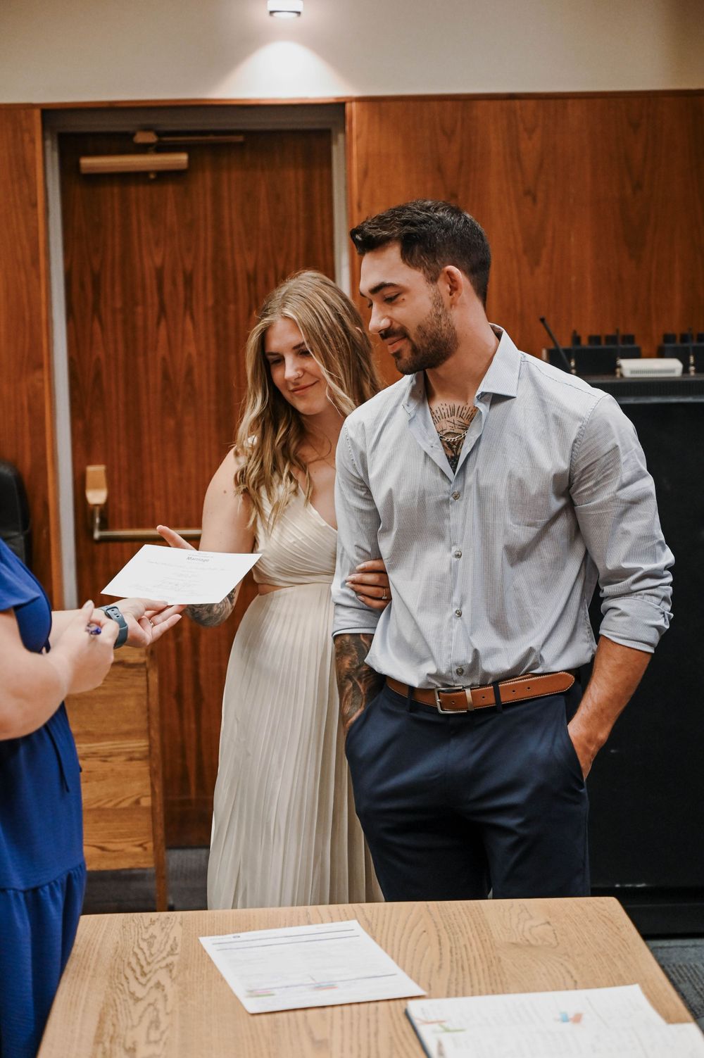 A couple smiles while reviewing paperwork at a wooden desk during what appears to be a courthouse ceremony.