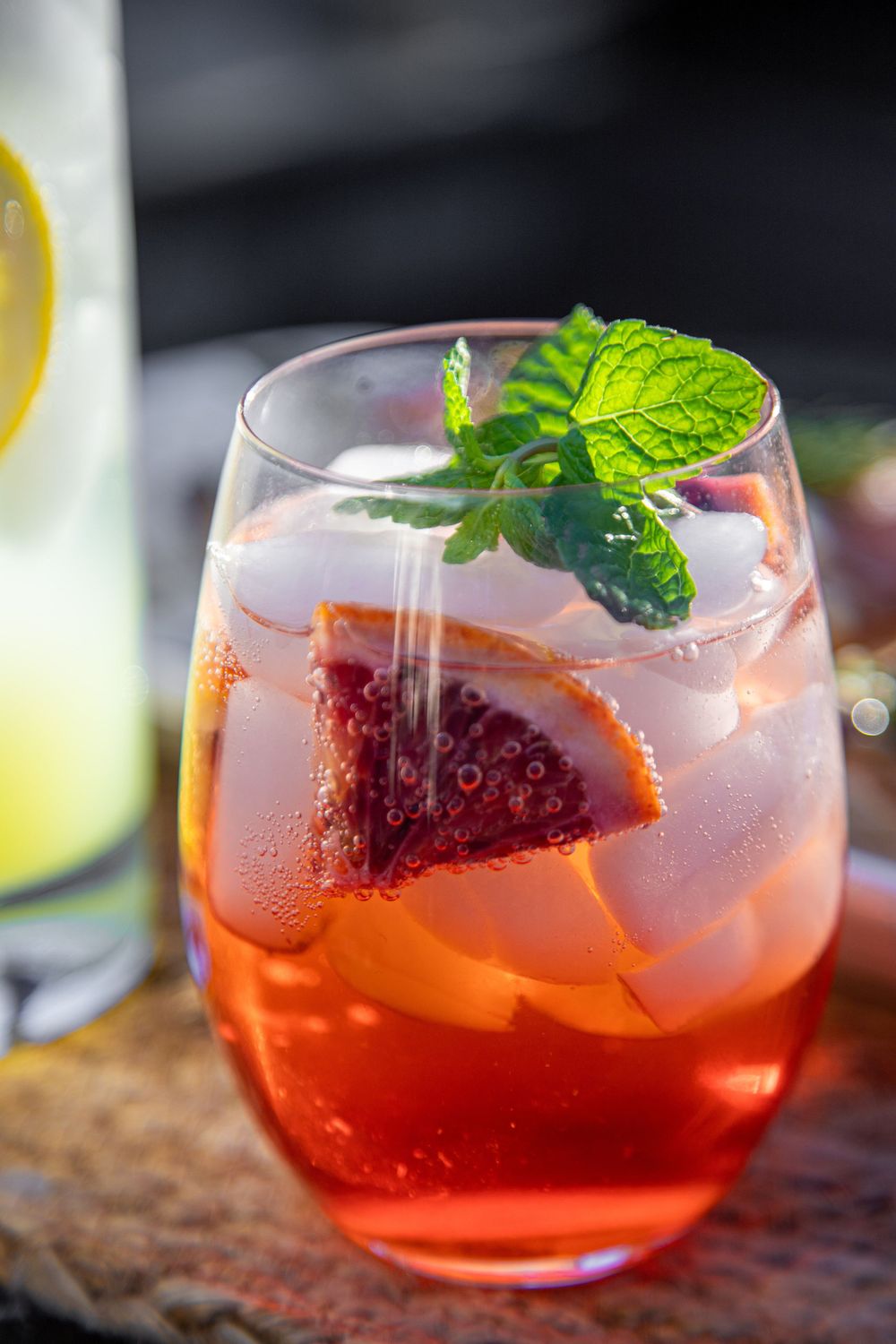 Close-up of aperol spritz garnished with blood orange slice and fresh mint leaves.