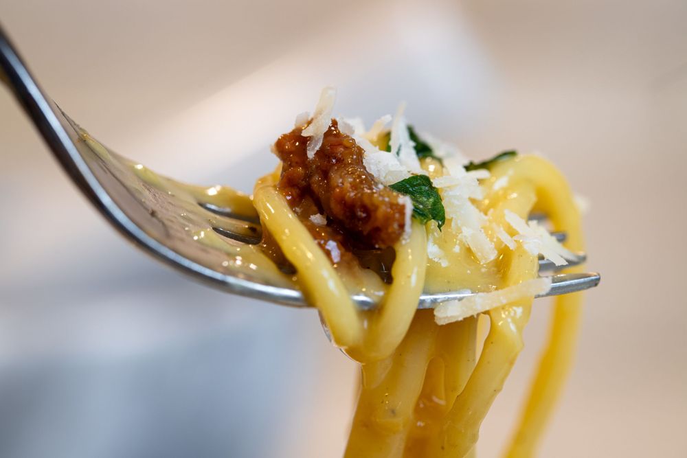 Fork twirling freshly cooked carbonara with guanciale and cheese garnished with basil.